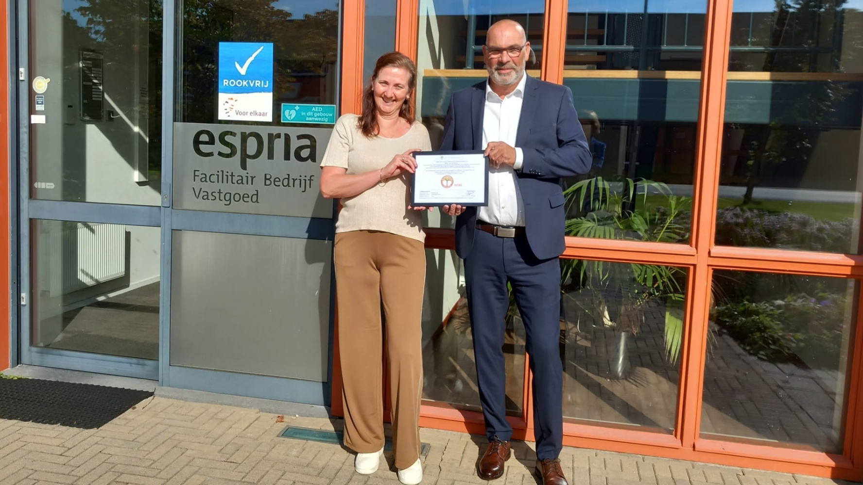 Medewerkers poseren met ingelijst bronzen certificaat voor het gebouw van Espria facilitair en inkoop